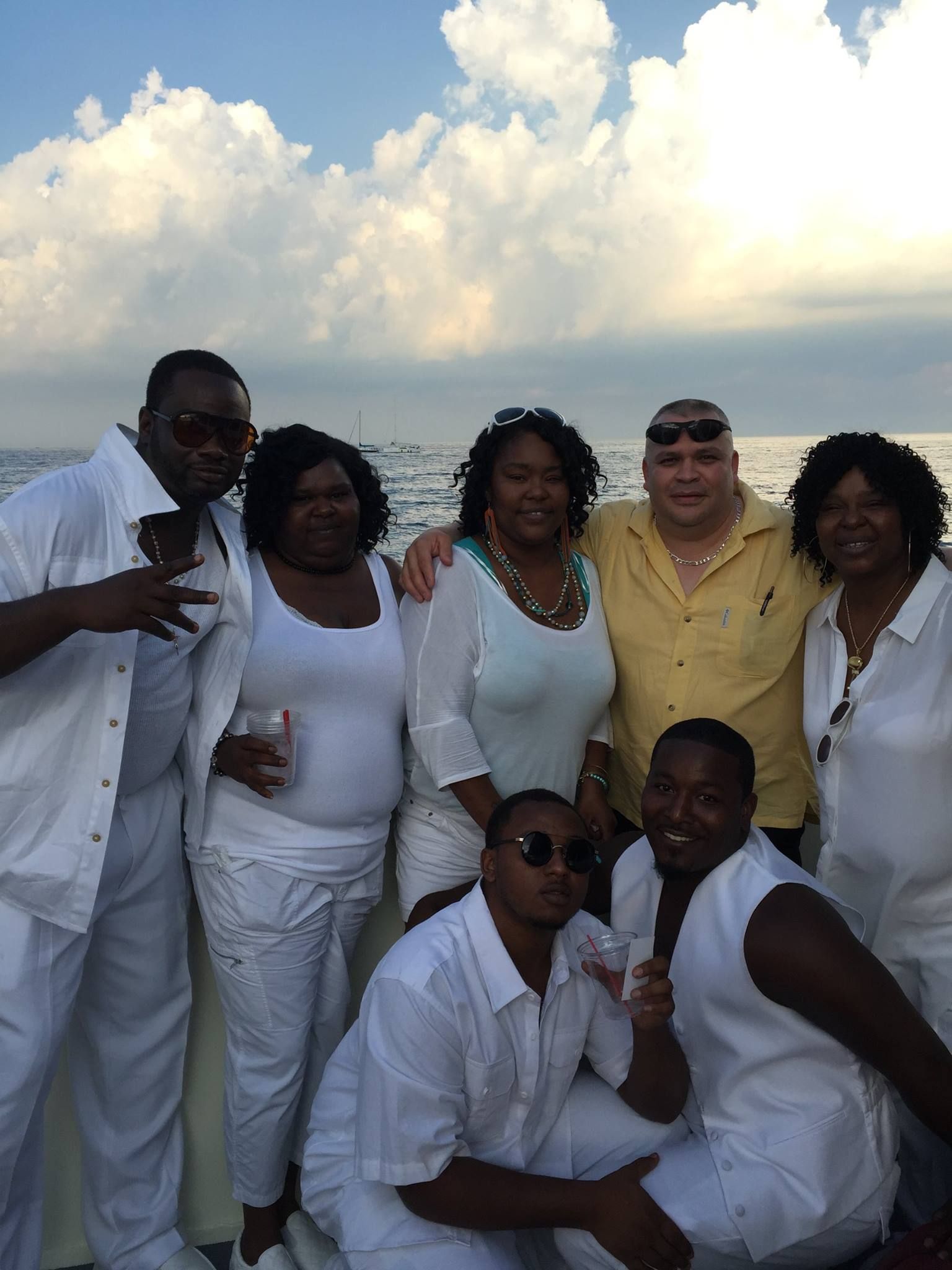 Group of six people in white and yellow outfits posing together outdoors against a bright cloudy sky