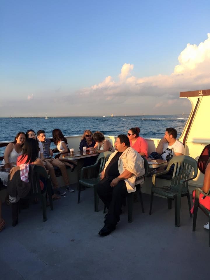People seated at a seaside deck table at sunset, with ocean and sky in the background.