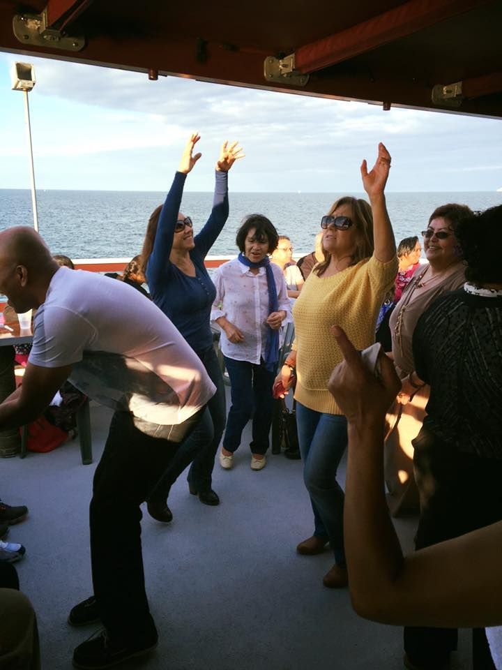 People dancing and raising their arms on a boat deck by the ocean in bright sunlight