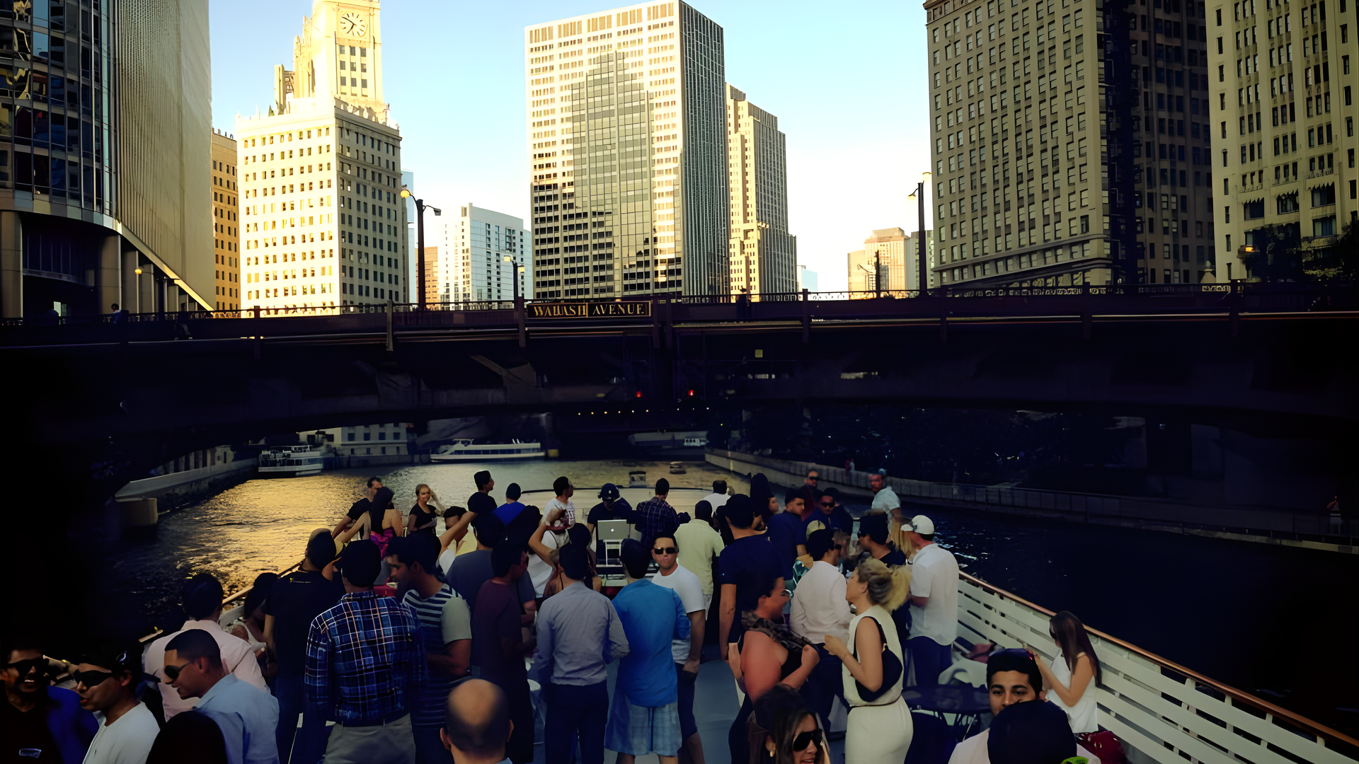 Crowded tour boat on a river between tall city buildings at sunset