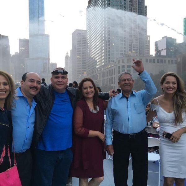 Group of people posing on a rooftop with city skyscrapers in the background, smiling and raising drinks