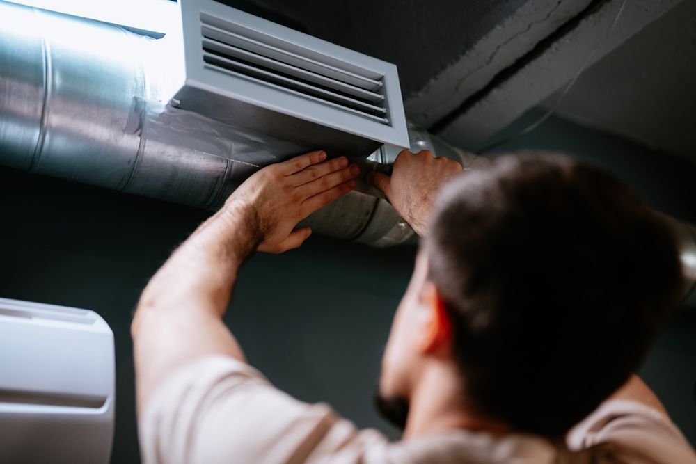 Worker adjusting a ceiling vent in a dark HVAC duct