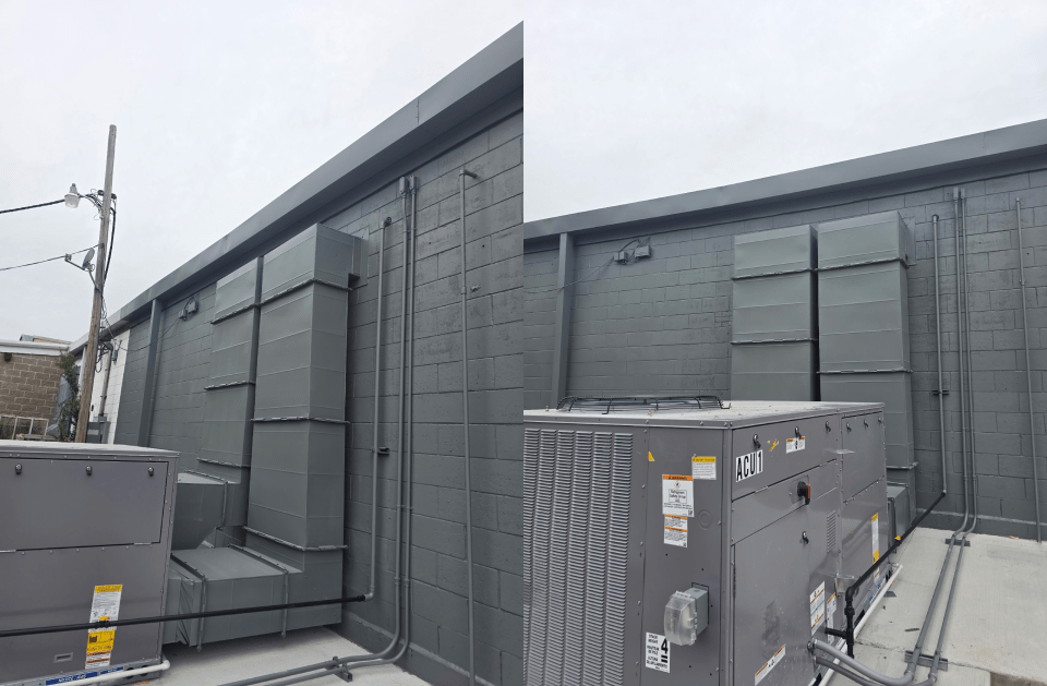Gray rooftop HVAC units beside a dark gray industrial building on an overcast day