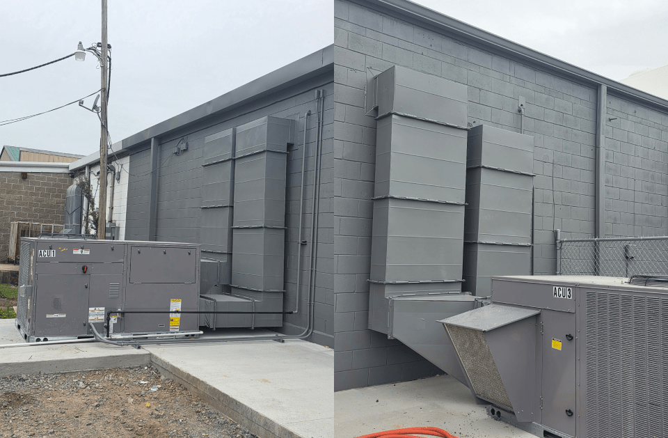 Gray industrial building exterior with large vents and rooftop HVAC units on a gravel lot