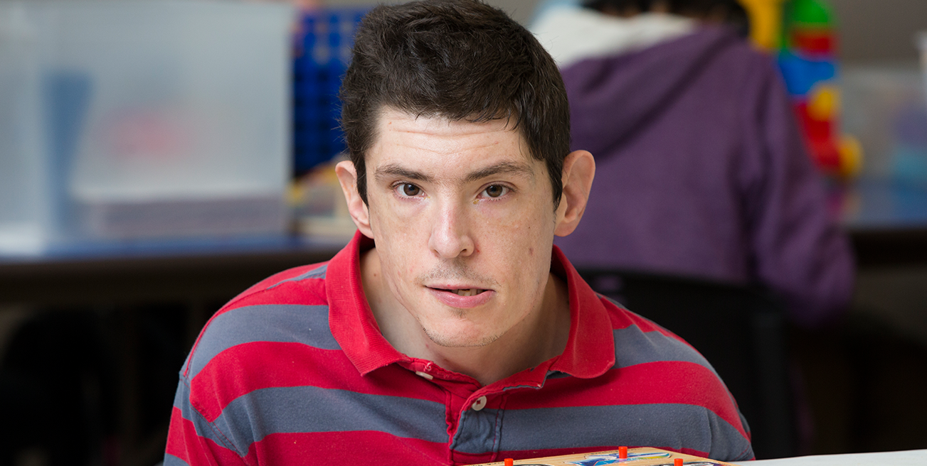 young adult male with disabilities smiling at a table with a puzzle in front of him