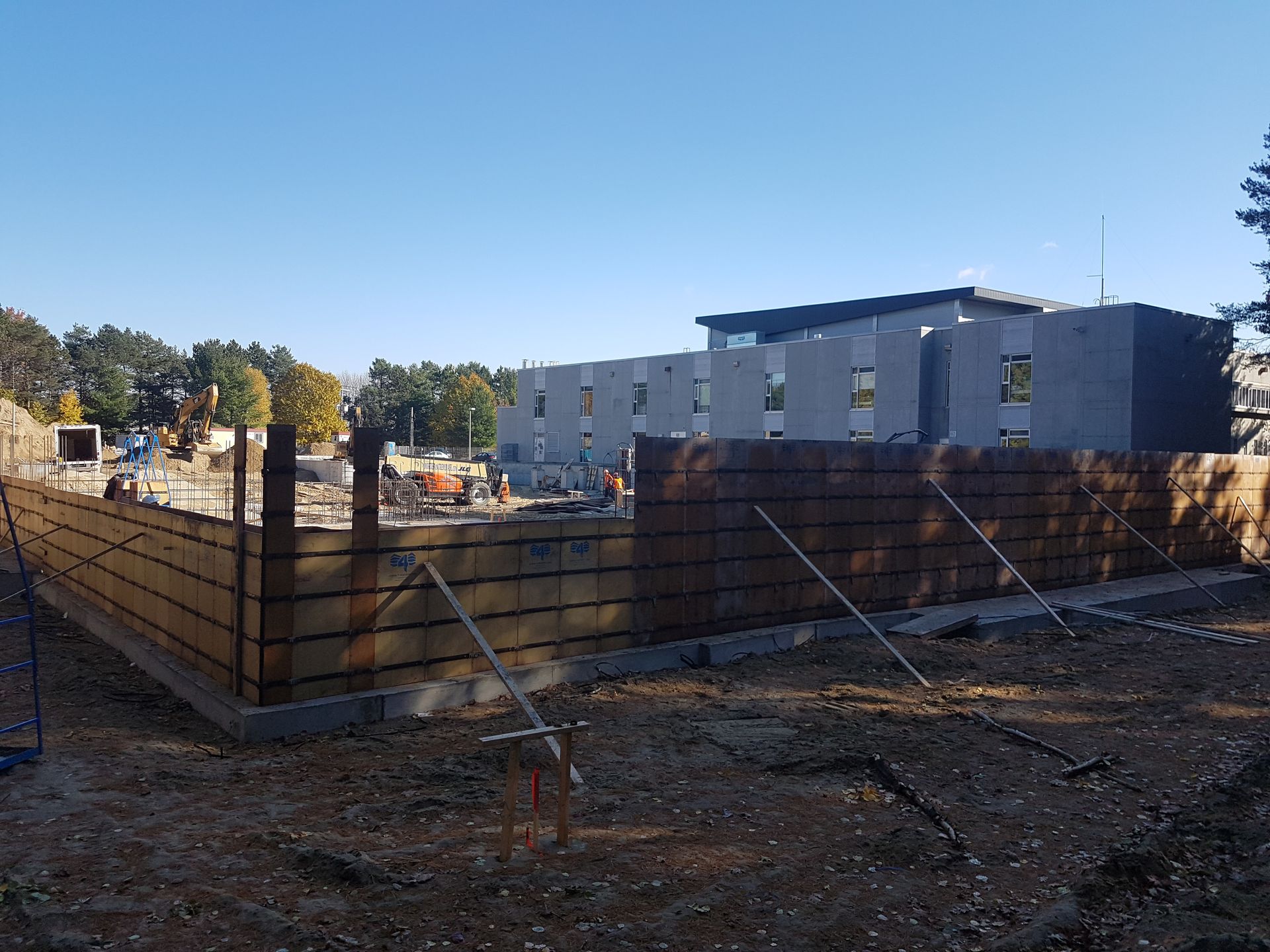 Un chantier de construction avec un bâtiment en arrière-plan et une clôture au premier plan.