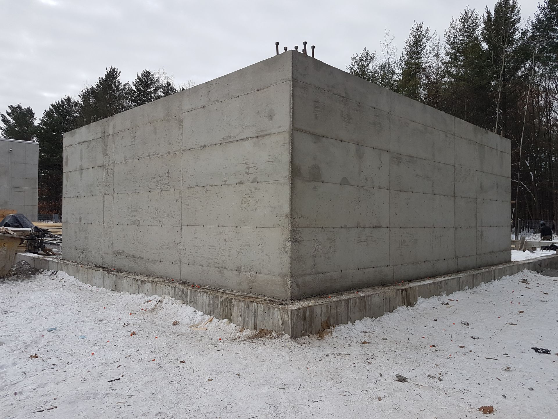 Un grand mur de béton est entouré de neige et d'arbres.