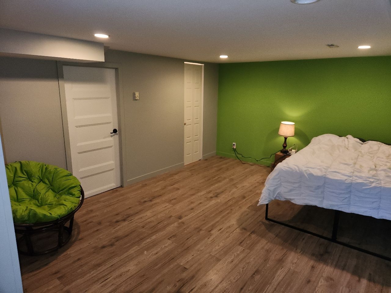 Une chambre avec un lit, une chaise, une lampe et des murs verts.