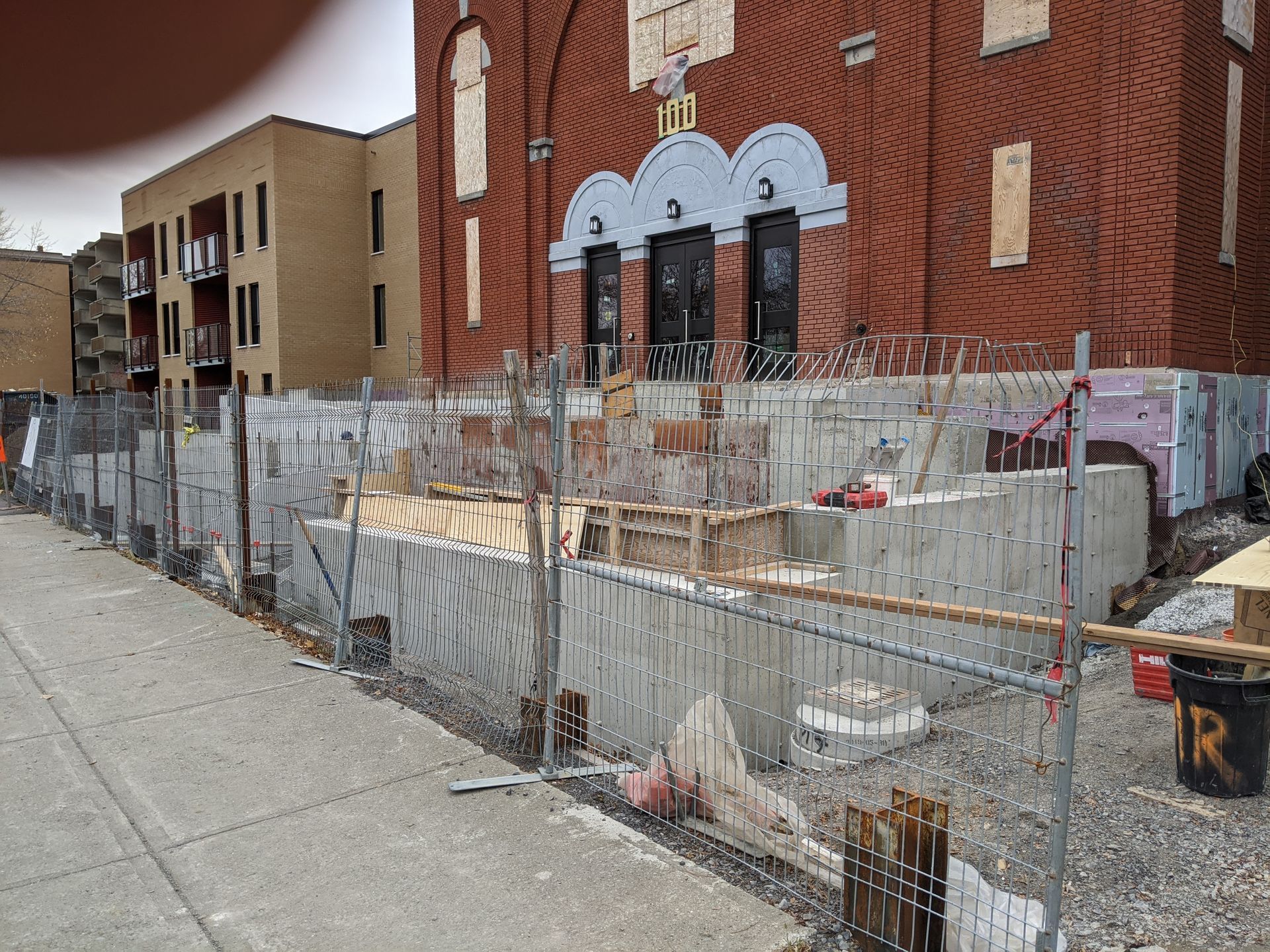 Une clôture entoure un chantier de construction avec un bâtiment en briques en arrière-plan.