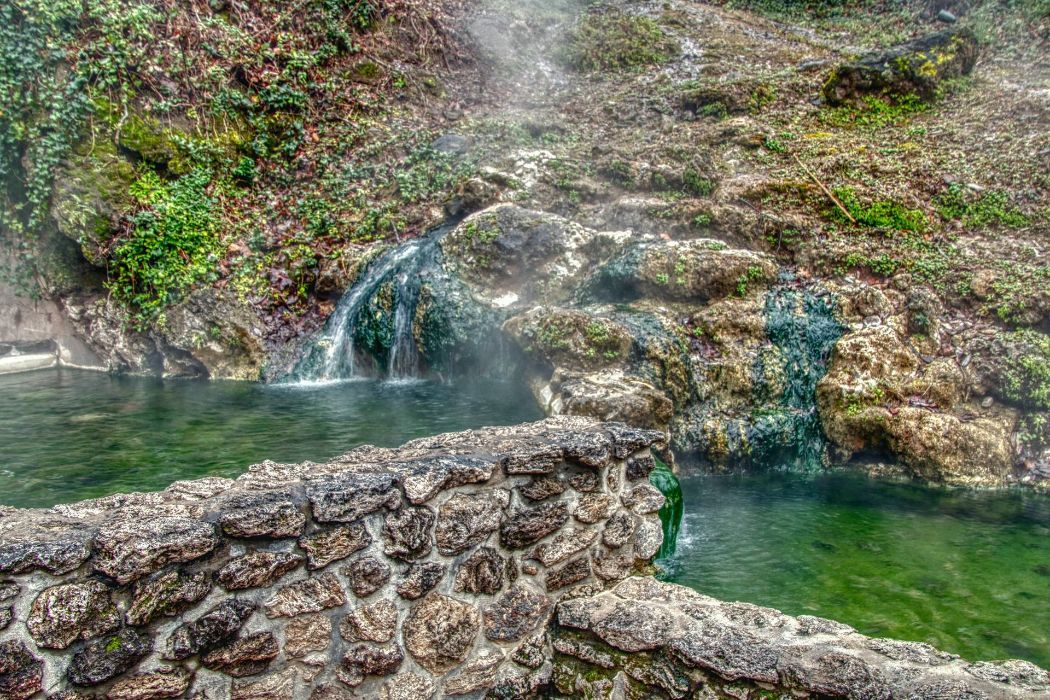 Hot springs cascading over mossy rocks; stone wall in foreground.