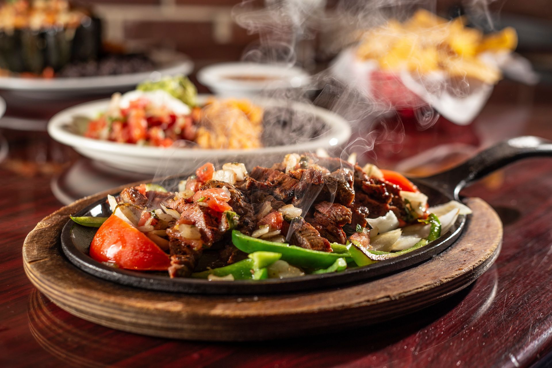 Sizzling fajitas on a cast iron skillet, with steam rising. Peppers, onions, and meat, in a restaurant setting.