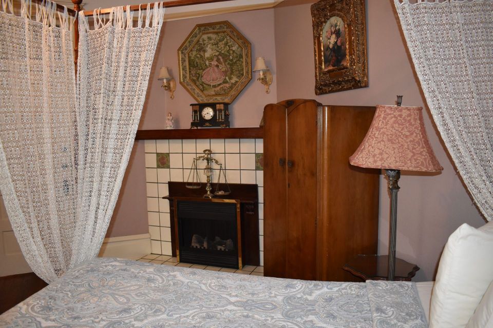 A bedroom with a fireplace, antique wardrobe, and a bed with lace curtains.