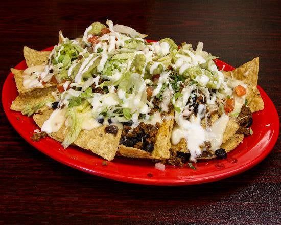 A red plate topped with nachos and toppings on a wooden table.