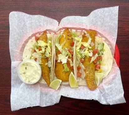 A basket of fish tacos with lettuce tomatoes and sour cream