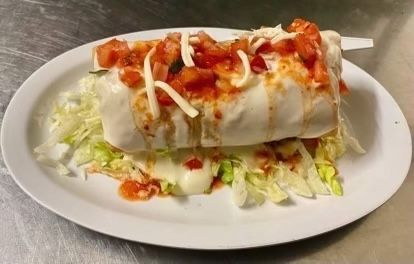 A burrito with lettuce , tomatoes and cheese on a white plate.