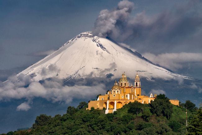 A church on top of a hill with a volcano in the background.