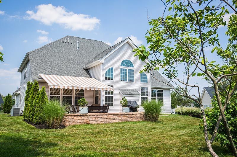 Two-story white house with a patio, awning, and a grassy backyard under a blue sky.