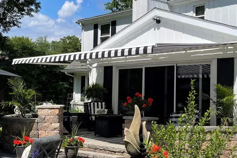 White house with black and white striped awning over sliding glass doors, sunny outdoor scene.