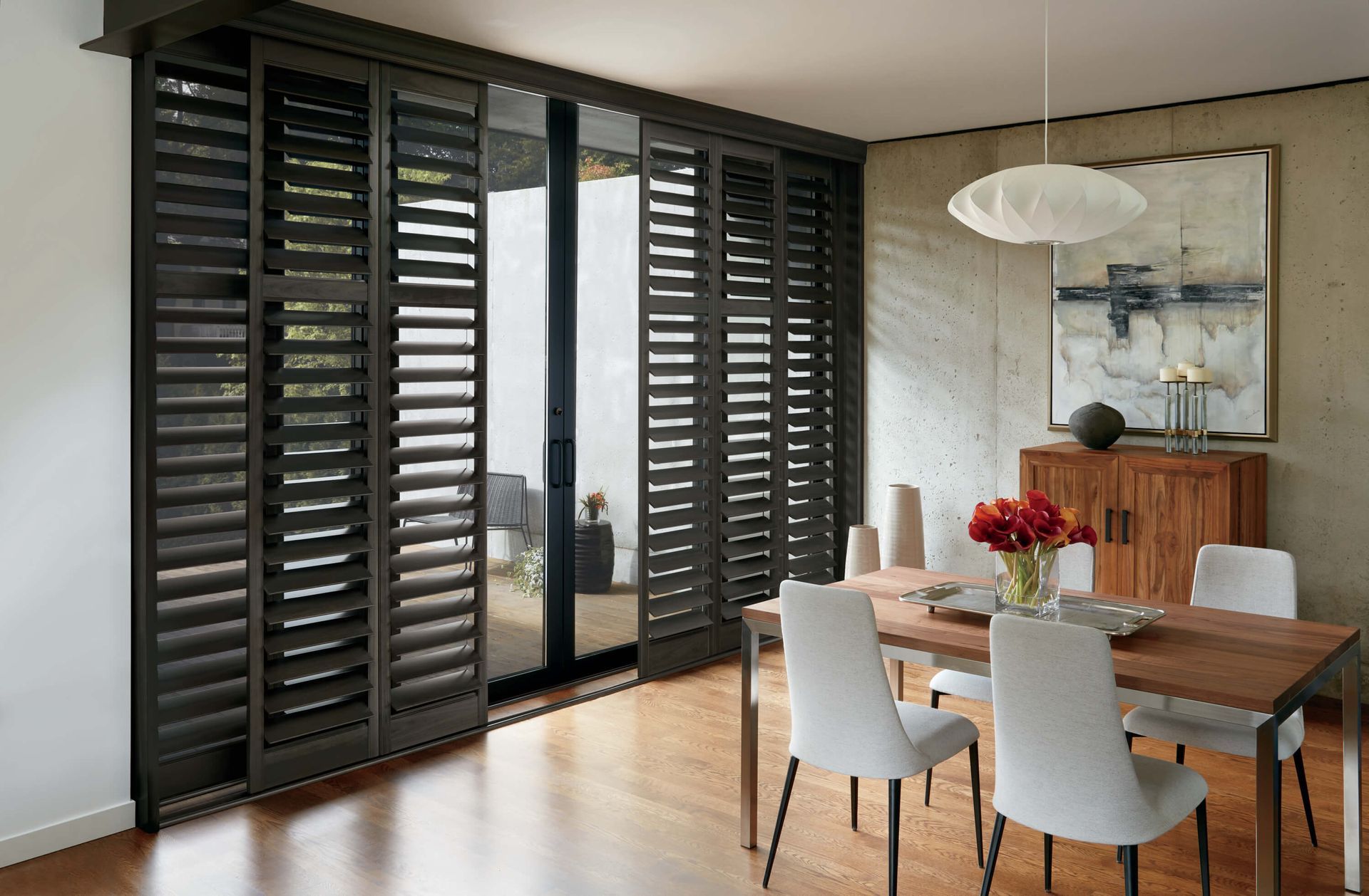 Dining room with dark shutters over sliding glass door, wooden table, and modern decor.