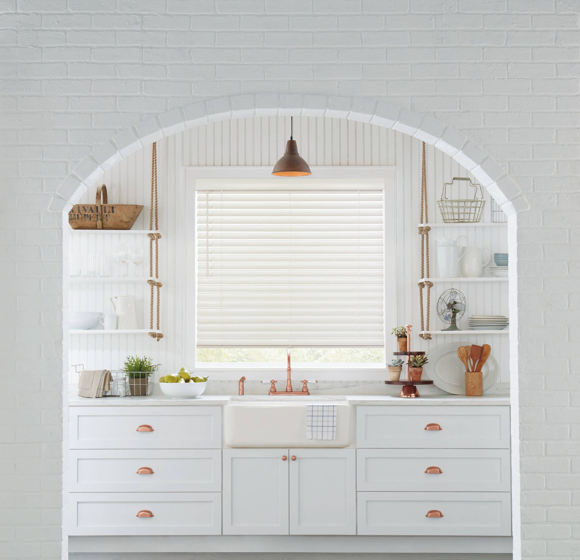 White kitchen with arched window, white cabinets, copper hardware, and a copper light fixture.