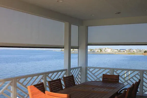 Patio with retractable sun shades overlooking a calm body of water; dining table and chairs visible.