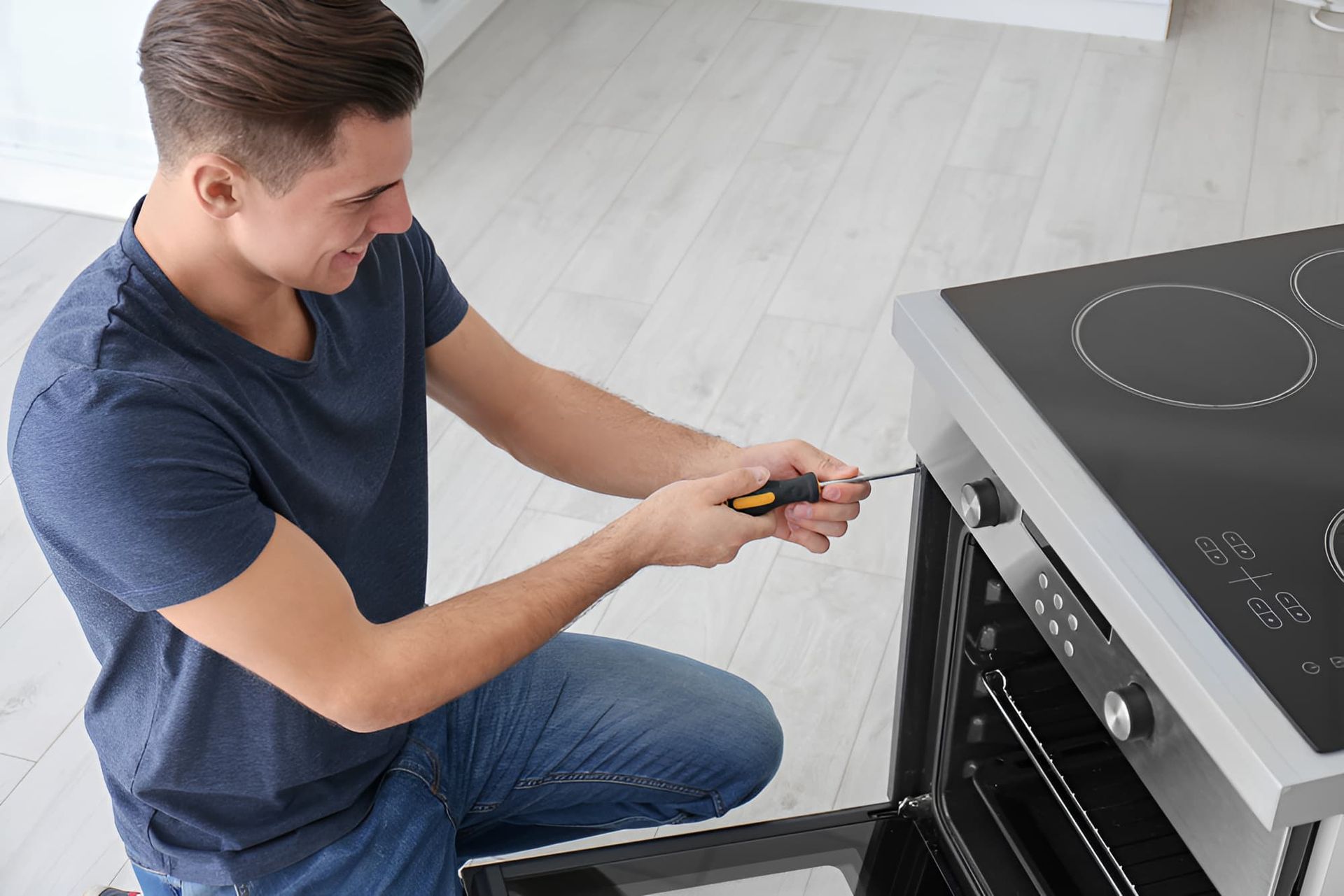 A Man Is Fixing An Oven With A Screwdriver In A Kitchen— Tweed Coast Appliance Repairs In Clothiers Creek, NSW