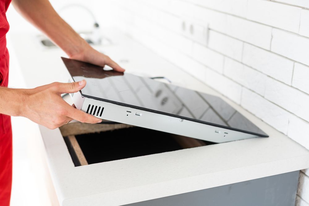 A Man Is Holding A Stove Top Oven In A Kitchen — Tweed Coast Appliance Repairs In Clothiers Creek, NSW