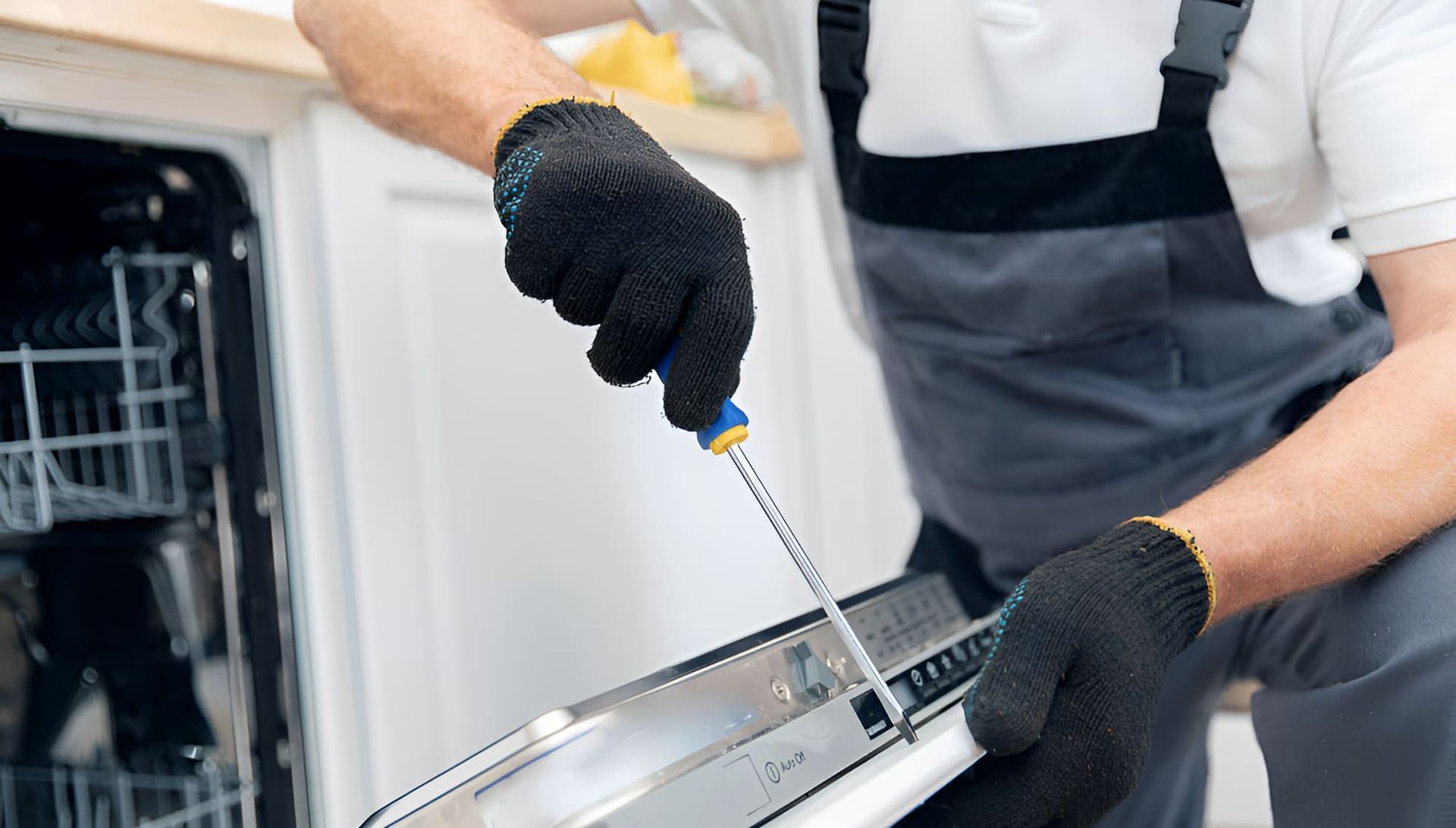 A Man Is Fixing A Dishwasher With A Screwdriver — Tweed Coast Appliance Repairs In Clothiers Creek, NSW