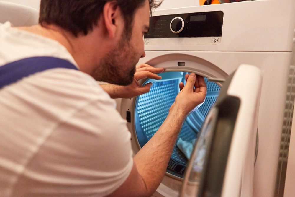 A Man Is Fixing A Washing Machine In A Laundry Room — Tweed Coast Appliance Repairs In Kingscliff, NSW