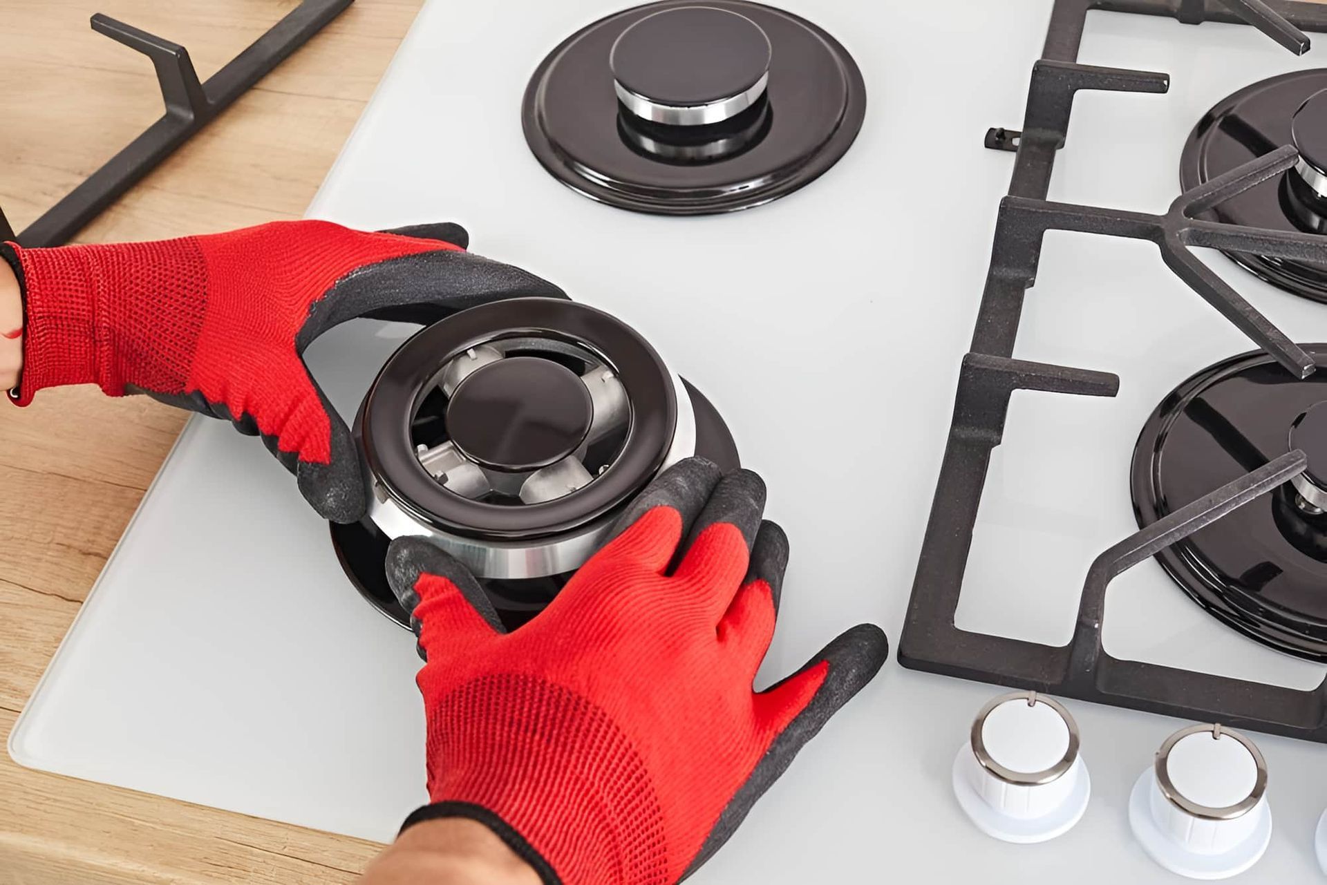 A Person Wearing Red Gloves Is Fixing A Gas Stove Burner — Tweed Coast Appliance Repairs In Murwillumbah, NSW