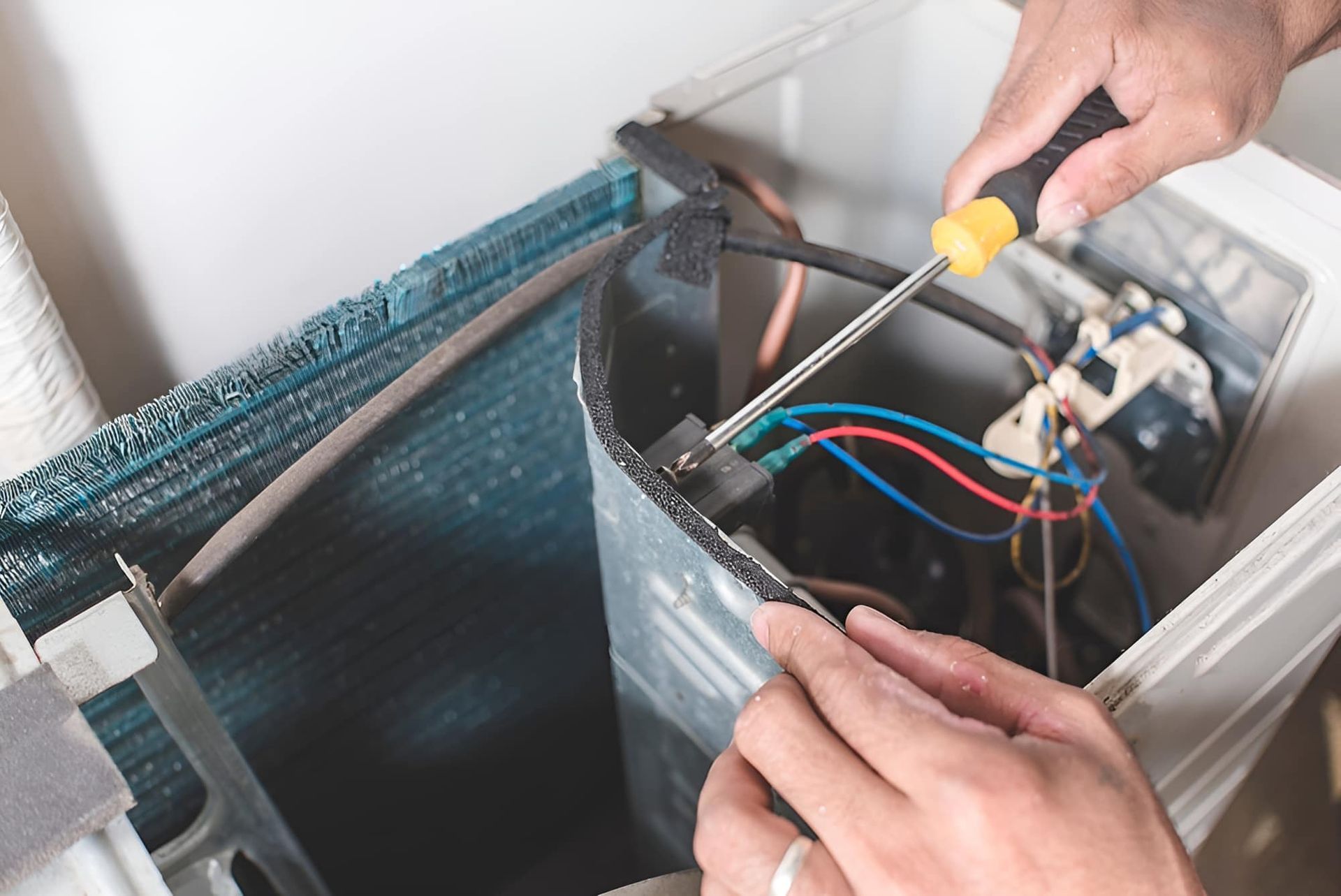 A Person Is Fixing An Air Conditioner With A Screwdriver — Tweed Coast Appliance Repairs In Tweed Heads, NSW