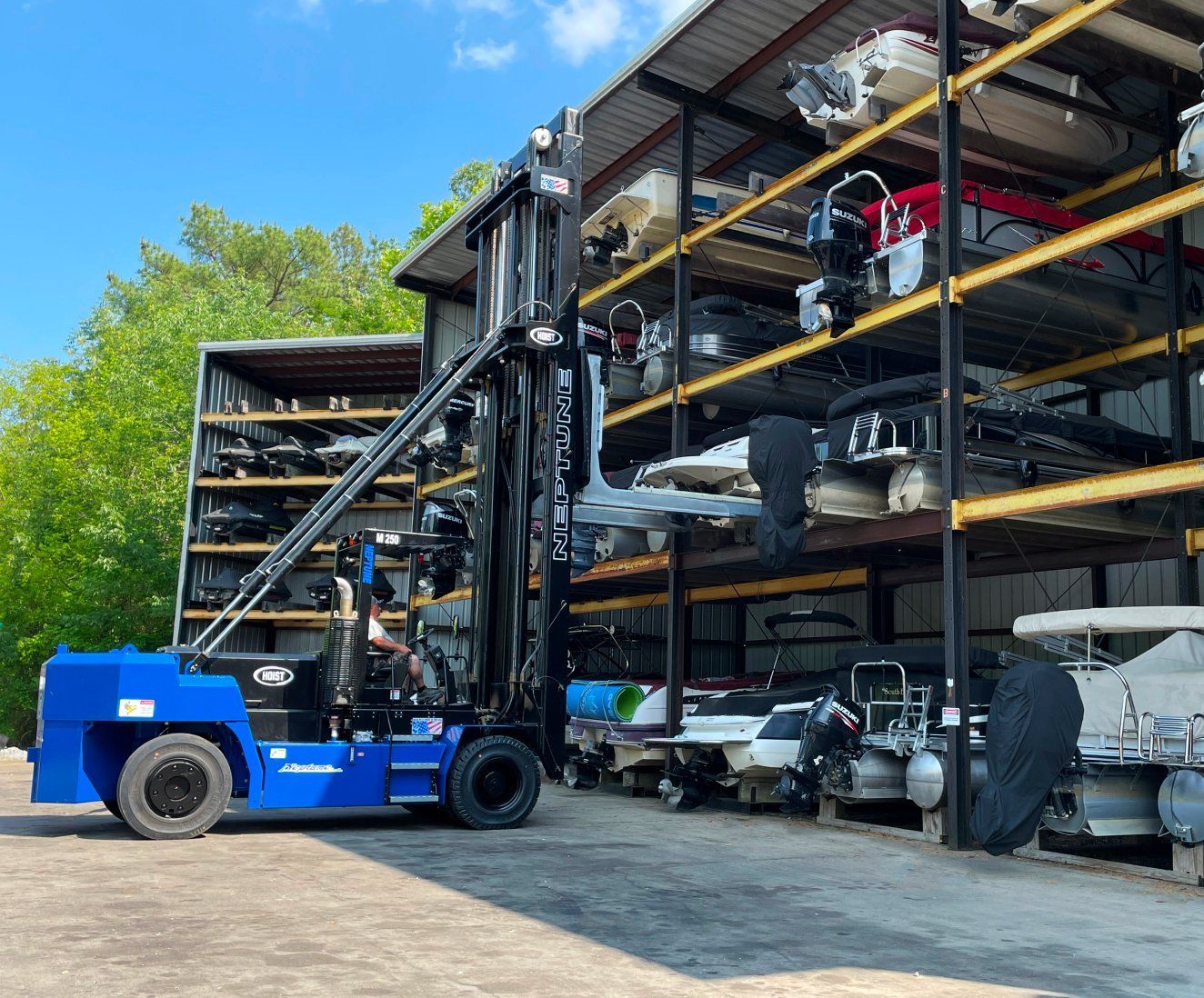 A blue forklift is parked in front of a warehouse full of boats