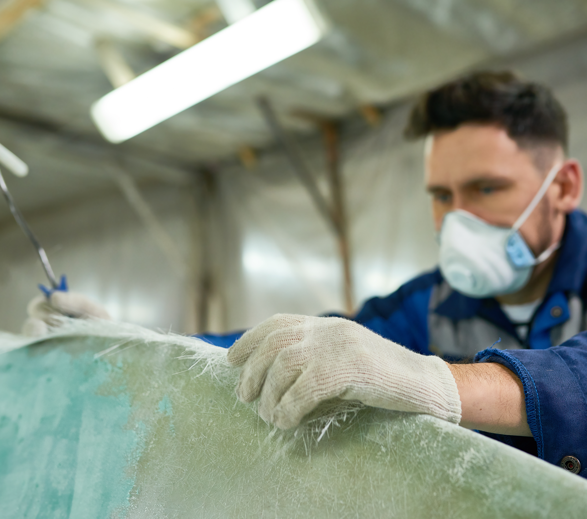 A man wearing a mask and gloves is working on a surfboard.