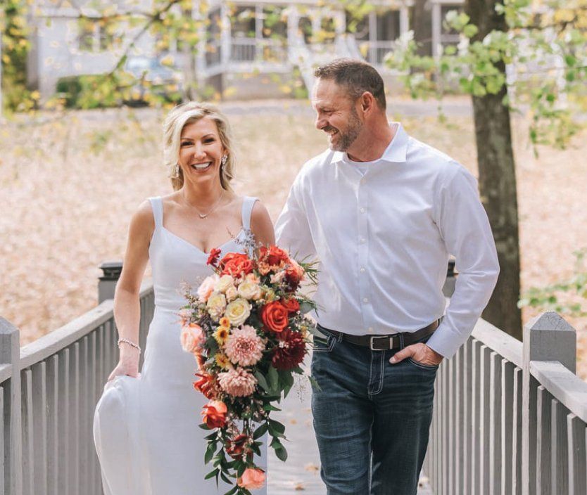 a bride and groom are walking across a bridge . the bride is holding a bouquet of flowers .