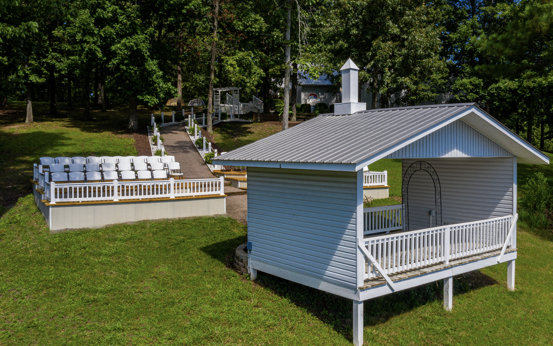 An aerial view of a small white house with a balcony in the middle of a grassy field.