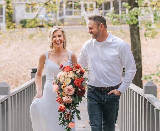 A bride and groom are walking across a bridge . the bride is holding a bouquet of flowers.