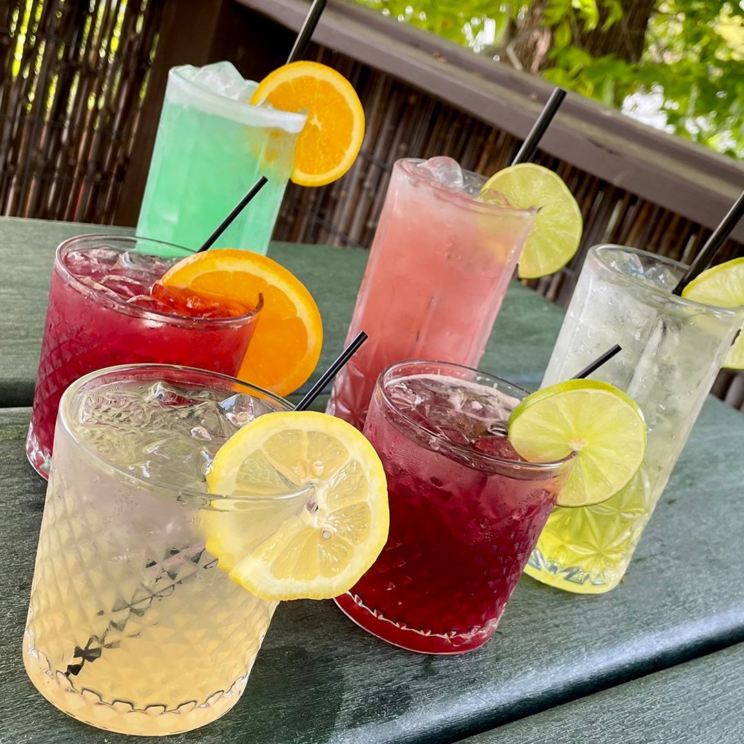 A table topped with a variety of drinks with lemon slices and straws.