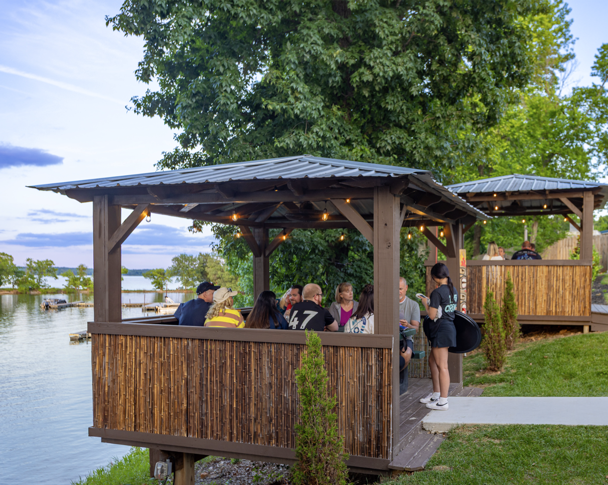 A group of people are sitting at a picnic table toasting with drinks.