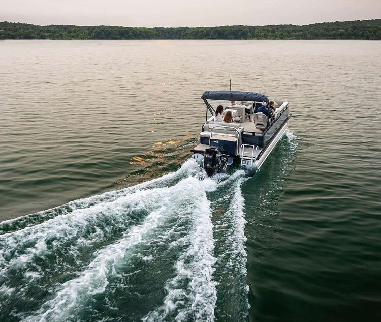 A row of pontoon boats are docked at a dock on a lake.