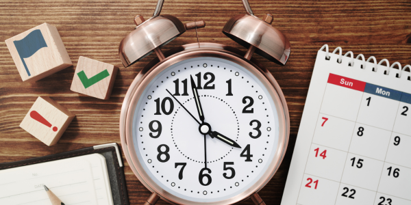 An alarm clock is sitting on a wooden table next to a calendar.