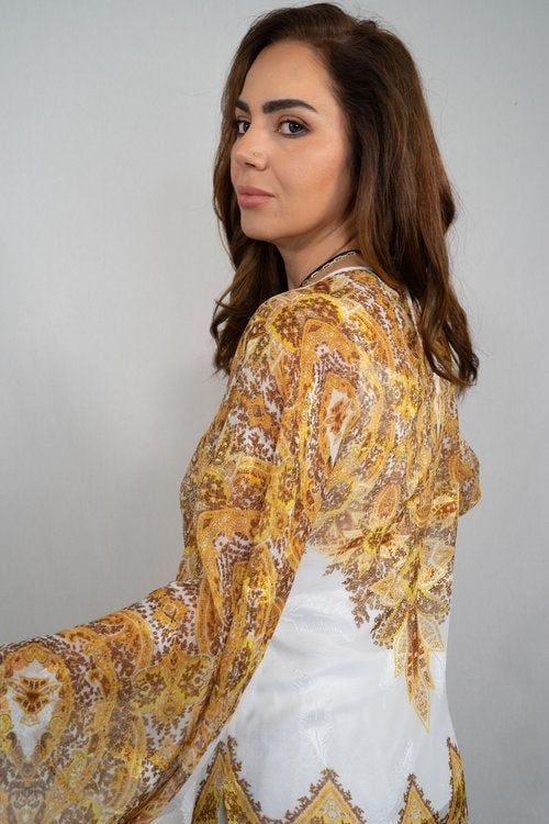 A woman in a white and gold dress is standing in front of a white wall.