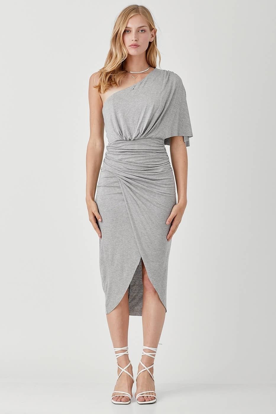 A woman is wearing a grey one shoulder dress and heels.