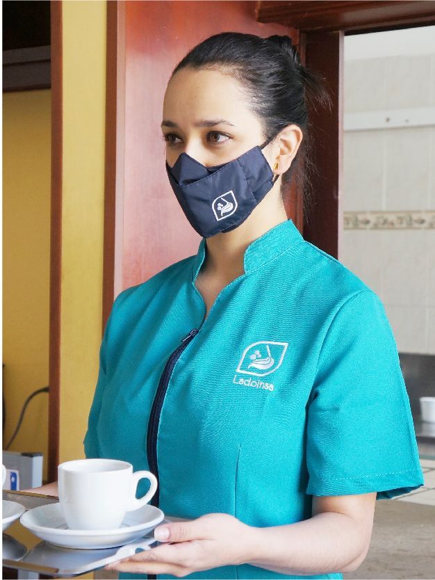 Una mujer que lleva una máscara sostiene una taza de café.