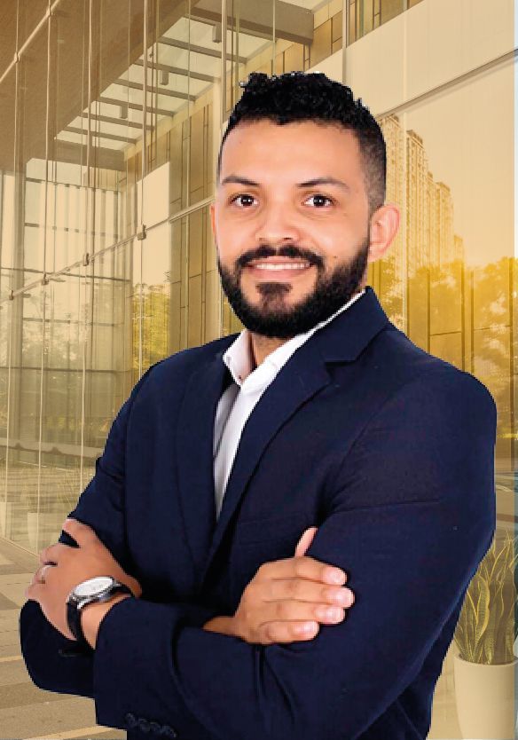 Un hombre con barba lleva traje y corbata y tiene los brazos cruzados.