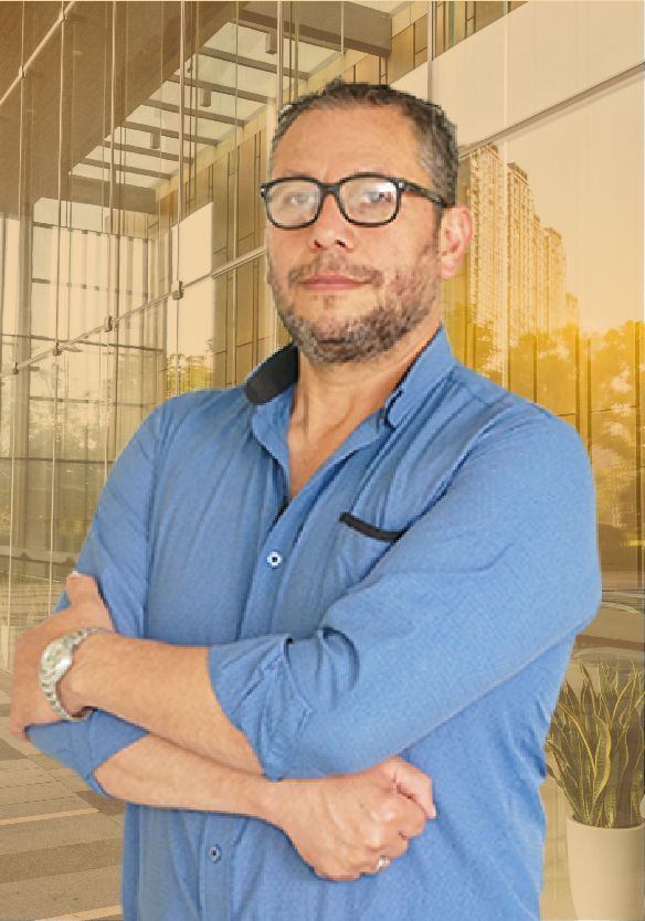 Un hombre que lleva gafas y una camisa azul está de pie con los brazos cruzados.