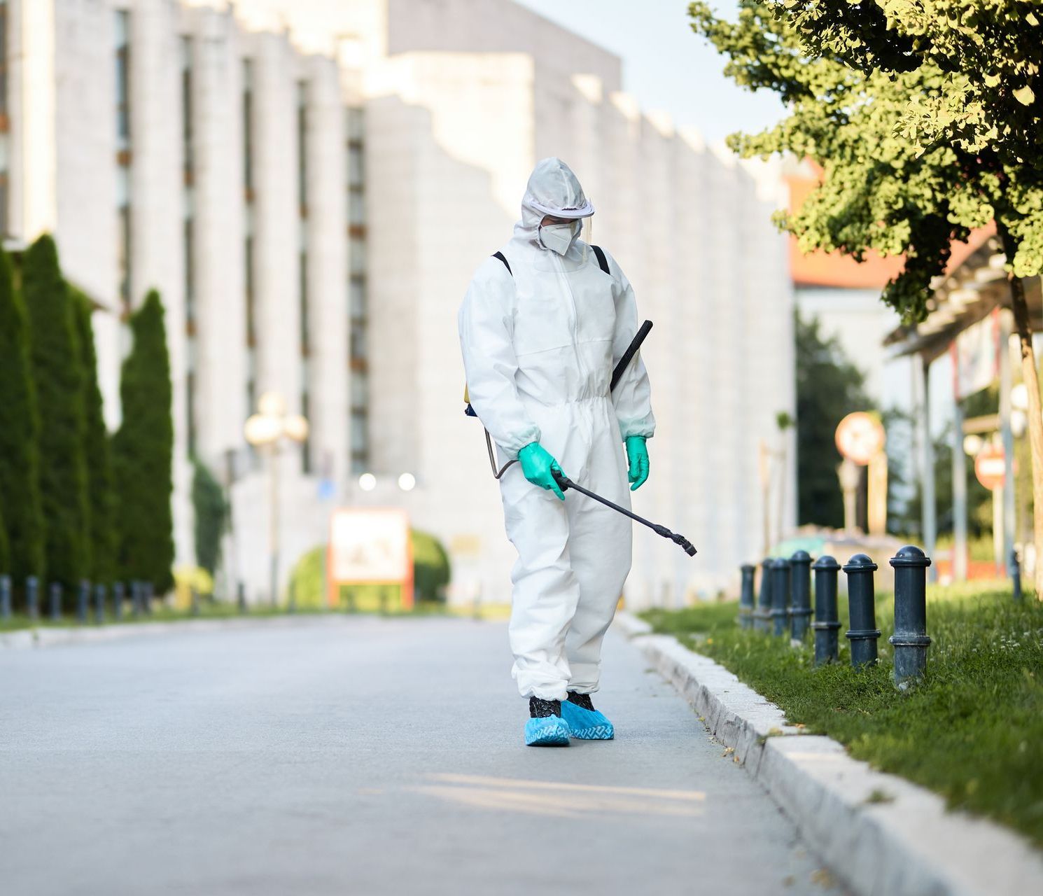 Un hombre con un traje de protección está rociando una calle con un pulverizador.