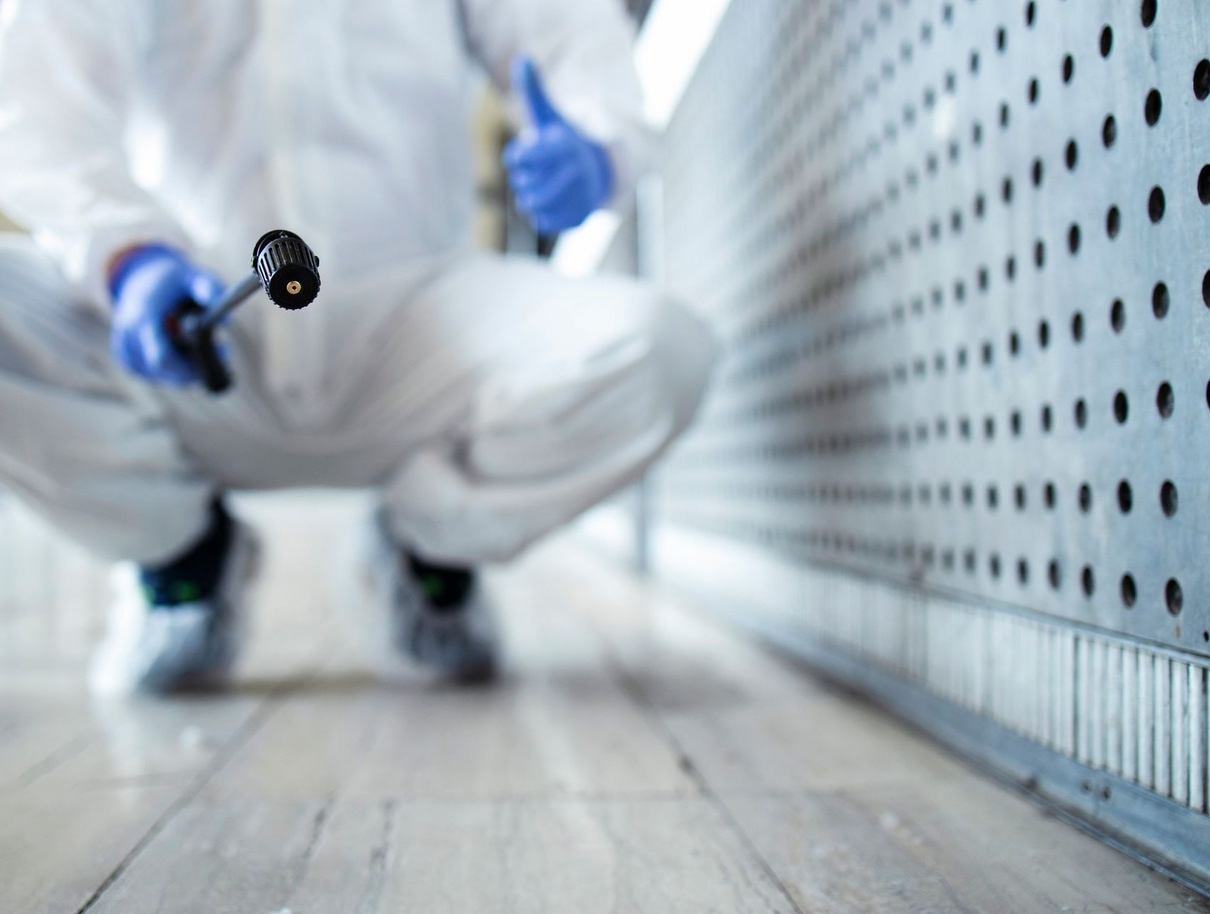 Una persona con un traje de protección está arrodillada en el suelo sosteniendo un pulverizador.