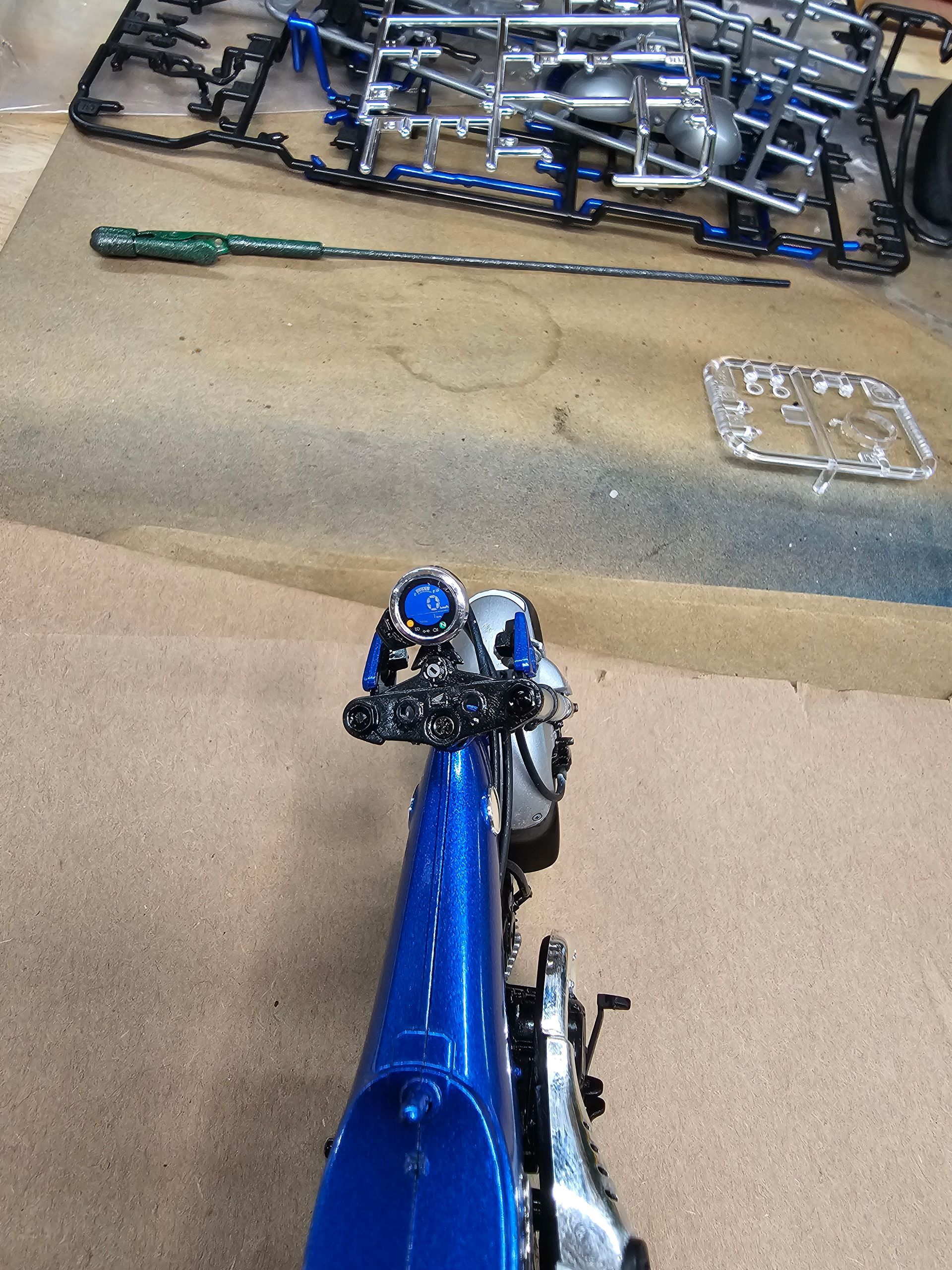Blue model motorcycle, tools, and parts on a light brown surface, likely a model kit.