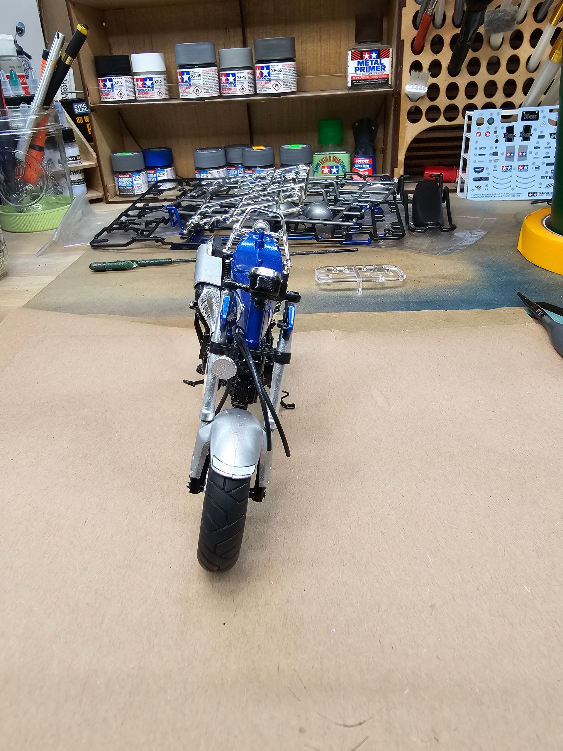 Miniature blue and silver motorcycle model on a work table, with parts and supplies visible in the background.