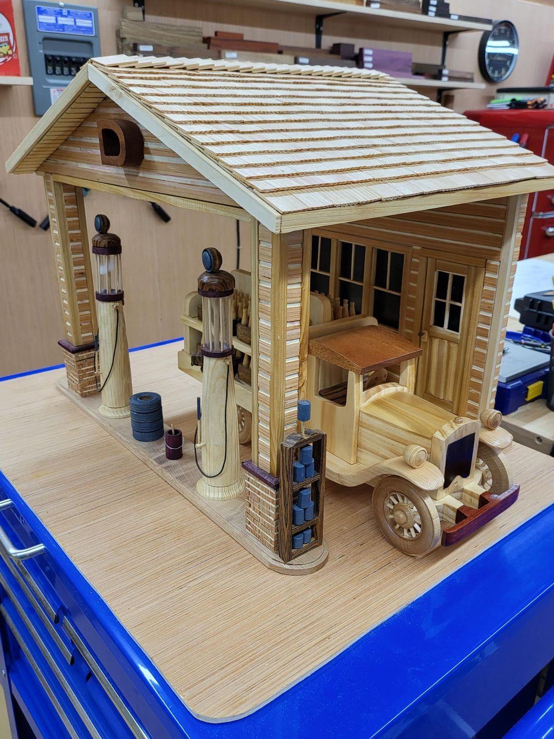 Wooden model of a vintage gas station with a truck inside; beige, brown, and blue colors.